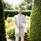 Groom in ice blue sherwani and white trousers, accessorized with off-white/cream suede Mojaris/Mojris, surrounded by trees