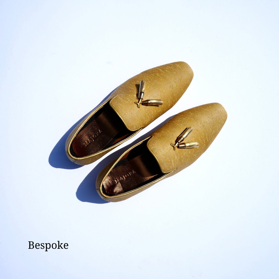 Bird's-eye view of a pair of gold mojari shoes with tassels. The insole features the word 'Majora' embossed in bronze/gold."
