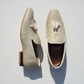 Cream suede Mojaris/Mojris with tassels, featuring gold insoles and embossed Majora logo. One shoe displayed on its side to showcase brown and black heel detailing