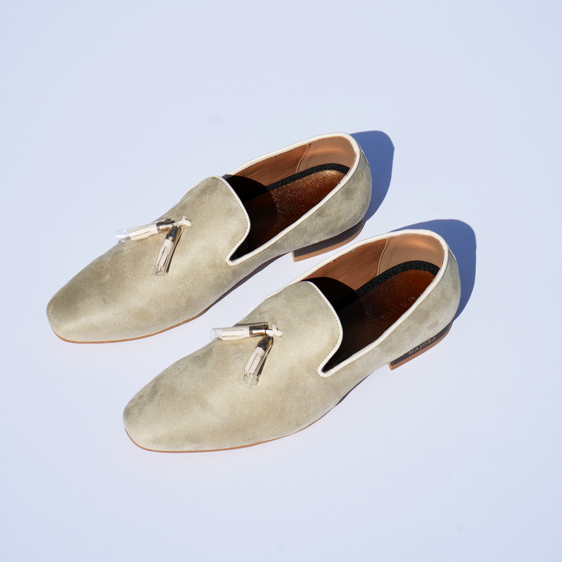 Cream suede men's Mojaris/Mojris with tassels, featuring gold insoles and embossed Majora logo, captured in sunlight.